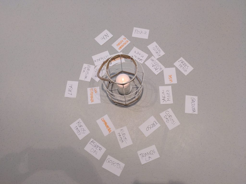 Una vela encendida y a su alrededor papeles con palabras escritas por las personas participantes en Auzotu.